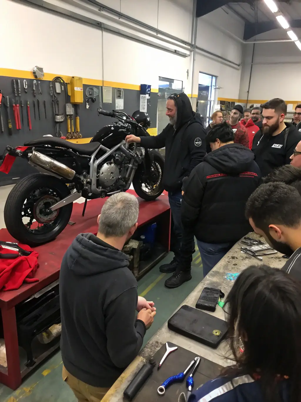 A group of teenagers working together to repair and maintain a motorcycle engine in a well-equipped garage. An instructor is overseeing their work, providing guidance and support.